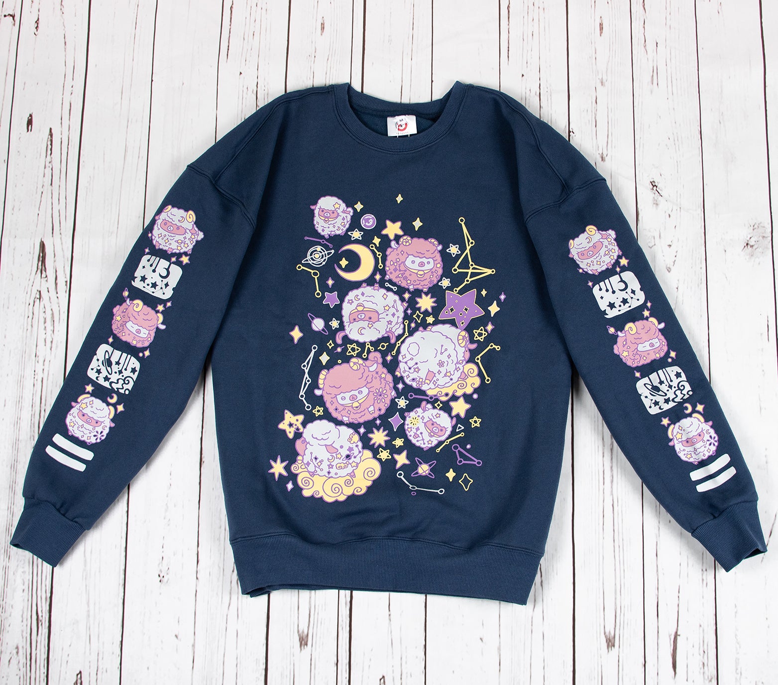 This thick navy colored sweatshirt features a front design of floating sheep in space, surrounded by starry skies and planets. The sweater is made of thick jersey fabric with a soft warm fleece interior. On both sleeves there is a column of floating sheep and starry sky elements that run down the entire sleeve. The sweatshirt comes in sizes XS to 2XL.