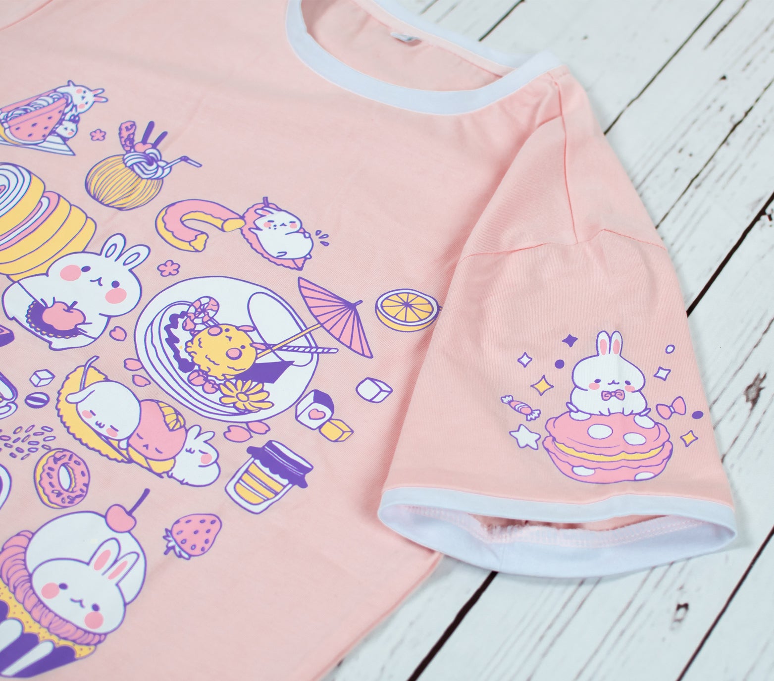 Light peach pink bunny t-shirt showing sweet bunny chefs making baking and café goods such as sweets, drinks, and desserts. The left sleeve of the shirt also shows a bunny sitting on a pink macraon. Light-weight and stretchable material that is made of 100% cotton. The collar and sleeve ends have cute white borders that truly frames the look of this summer shirt. Available in sizes XXS to 2XL.
