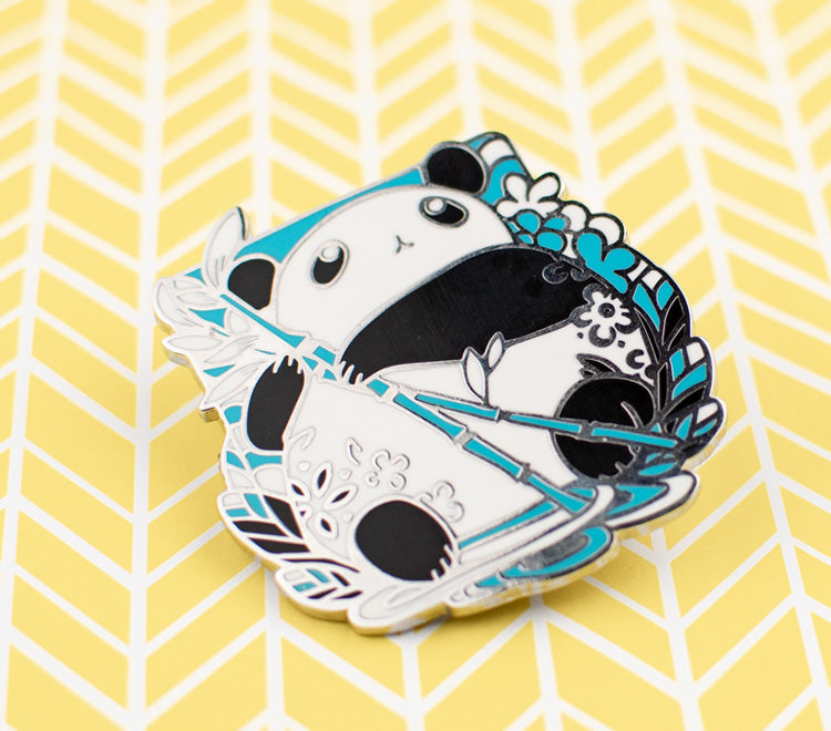 The pin design features a chibi panda holding a bamboo stem and looking up. The pin is printed on silver metal and has two rubber back pins in place for you to attach the pin to your clothes, bags, etc.