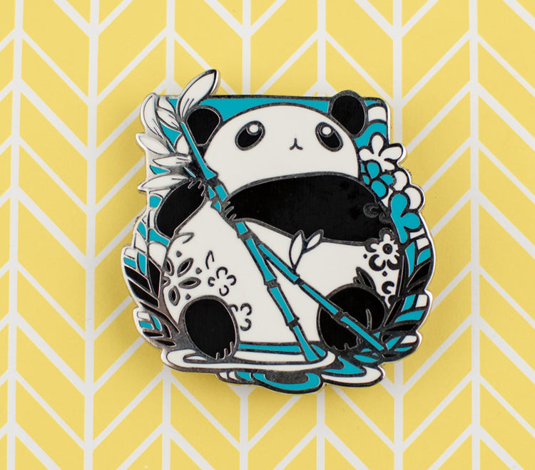 The pin design features a chibi panda holding a bamboo stem and looking up. The pin is printed on silver metal and has two rubber back pins in place for you to attach the pin to your clothes, bags, etc.