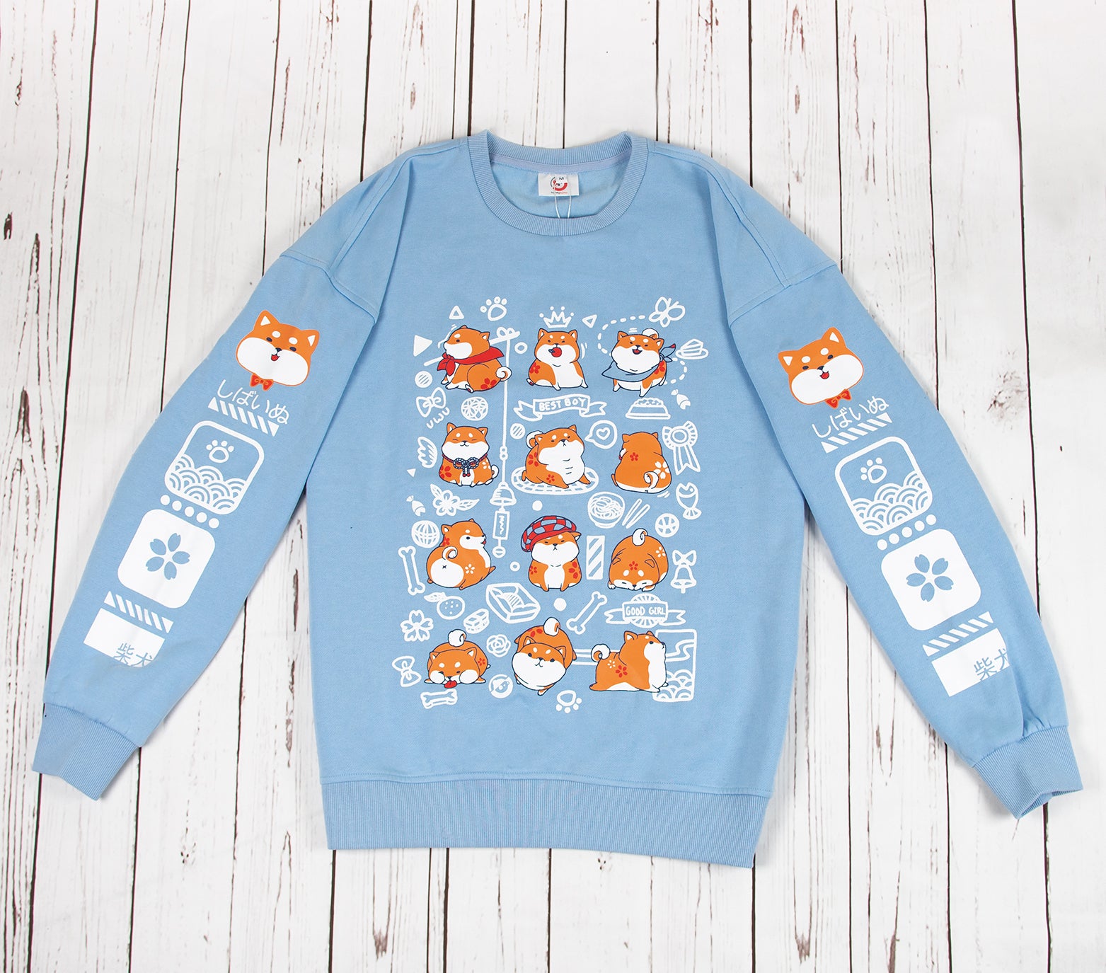This light blue sweatshirt features a front design of a group of shiba inu in various adorable poses. The design captures the various antics of the shiba inu. Both sleeves also feature designs that run down the sleeves, which matches the front main design of the sweatshirt. The material is medium heavy jersey style with a soft fleece interior. The sweatshirt comes in sizes from XXS to 2XL.