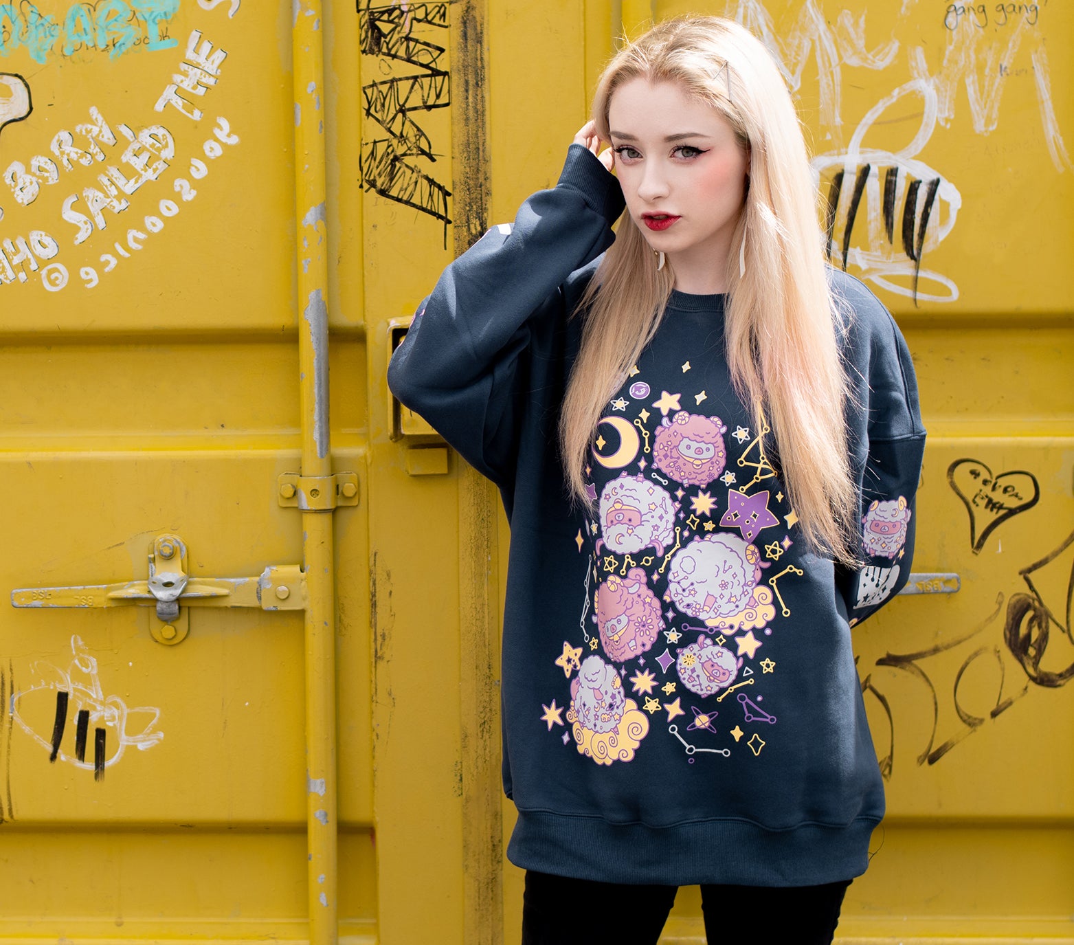 This thick navy colored sweatshirt features a front design of floating sheep in space, surrounded by starry skies and planets. The sweater is made of thick jersey fabric with a soft warm fleece interior. On both sleeves there is a column of floating sheep and starry sky elements that run down the entire sleeve. The sweatshirt comes in sizes XS to 2XL.